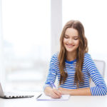 Une jeune femme suit une formation en langue en ligne en prenant des notes