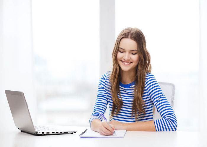 Une jeune femme suit une formation en langue en ligne en prenant des notes