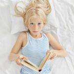 Une fillette lit un livre en anglais sur son lit