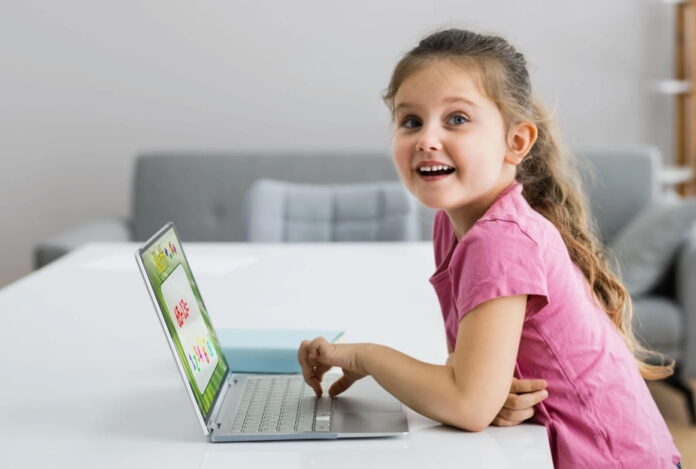 Défis cours à distance Enfant Une enfant sourit en apprenant l'anglais avec un cours sur son écran d'ordinateur