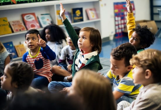 Un petit groupe d'enfants d'école primaire lèvent la main pour participer en anglais.
